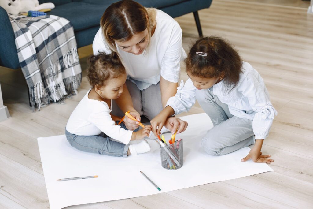 A mother and her children engage in a fun and creative coloring activity on the floor.