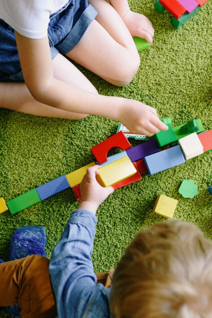 Children engaged in playful activities with vibrant blocks on a green carpet.