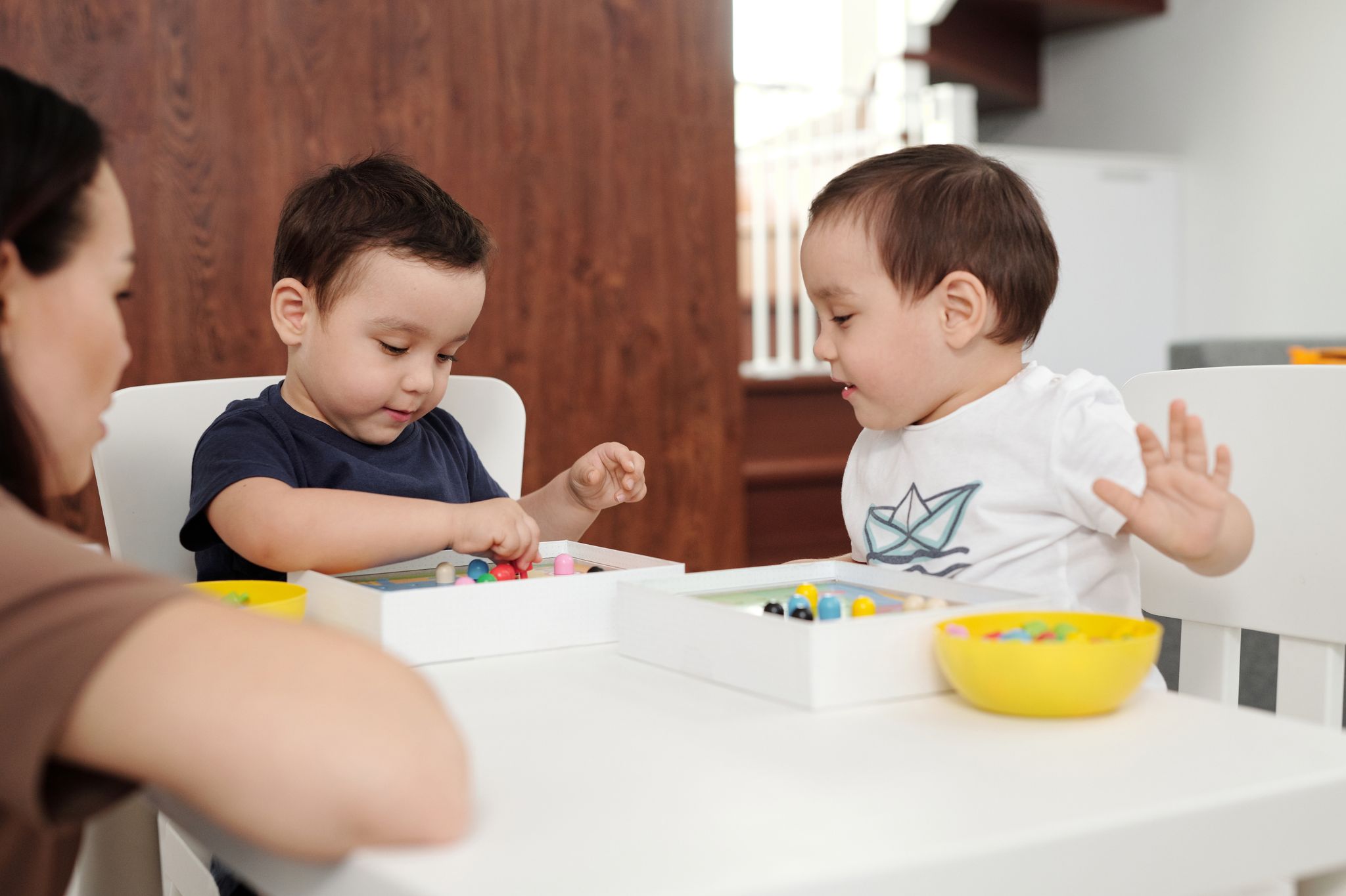 Two children playing with toys under the supervision of their mother in a cozy home setting.
